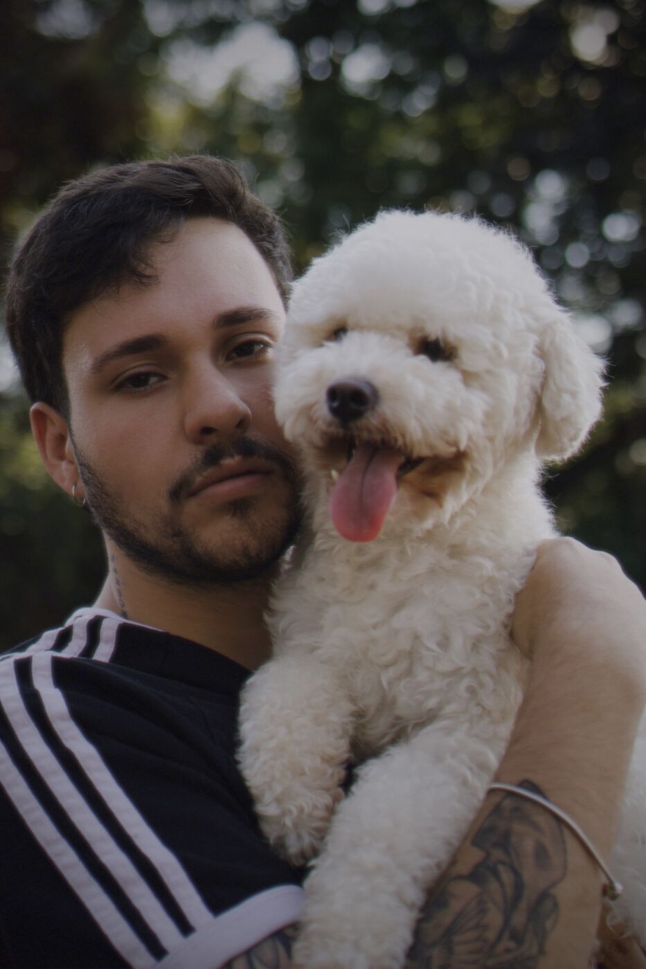 Homem abraçado a um poodle branco com fundo de folhas desfocadas